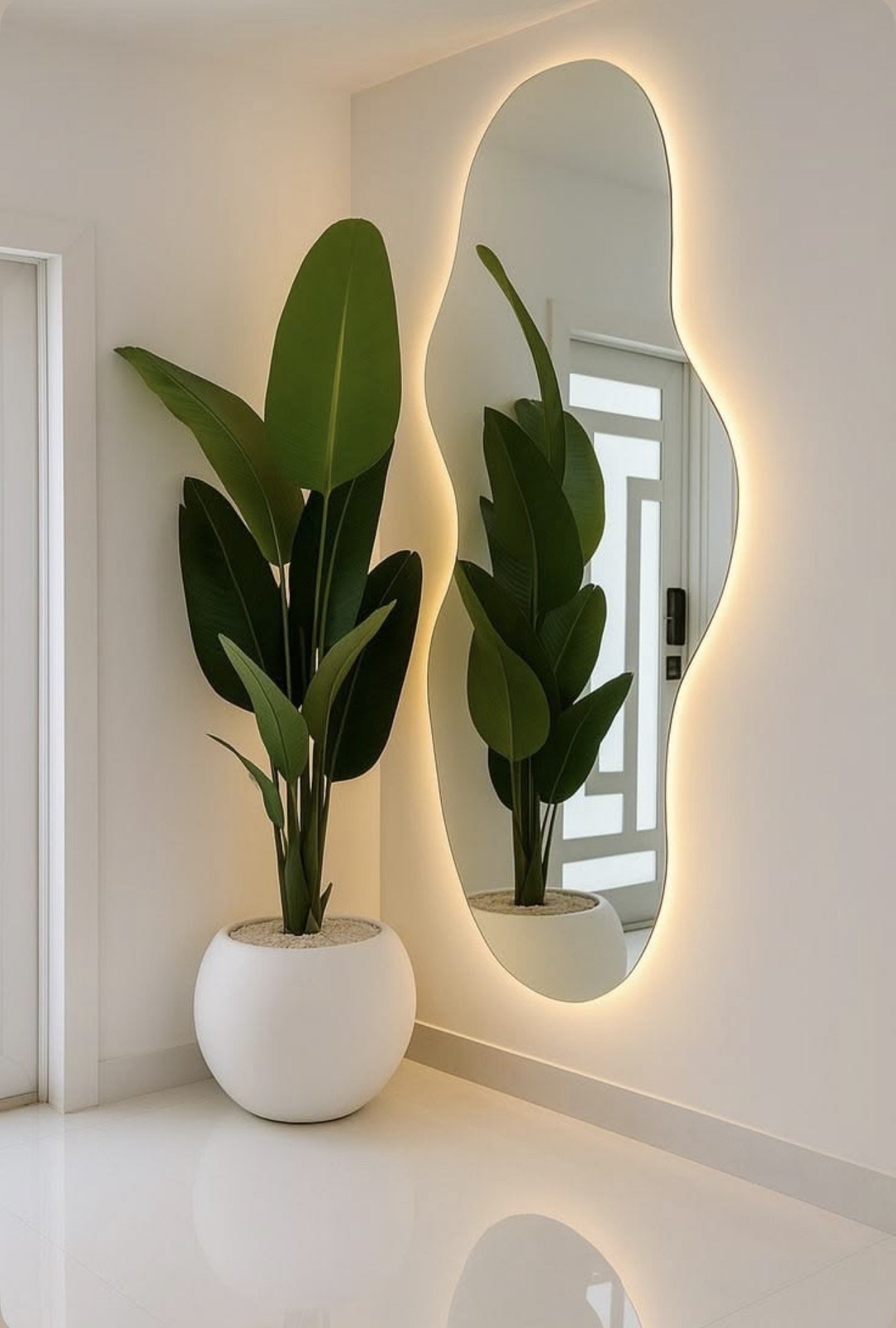 A clean cream entryway with an organic backlit mirror, a tall green plant in a white planter, and warm light around the mirror.